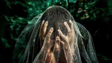 A person sits with their head in their hands, draped in a translucent veil speckled with water droplets. The background swirls with deep green hues, creating a sense of emotional intensity and isolation. The image evokes feelings of overwhelm, vulnerability, and quiet struggle.
